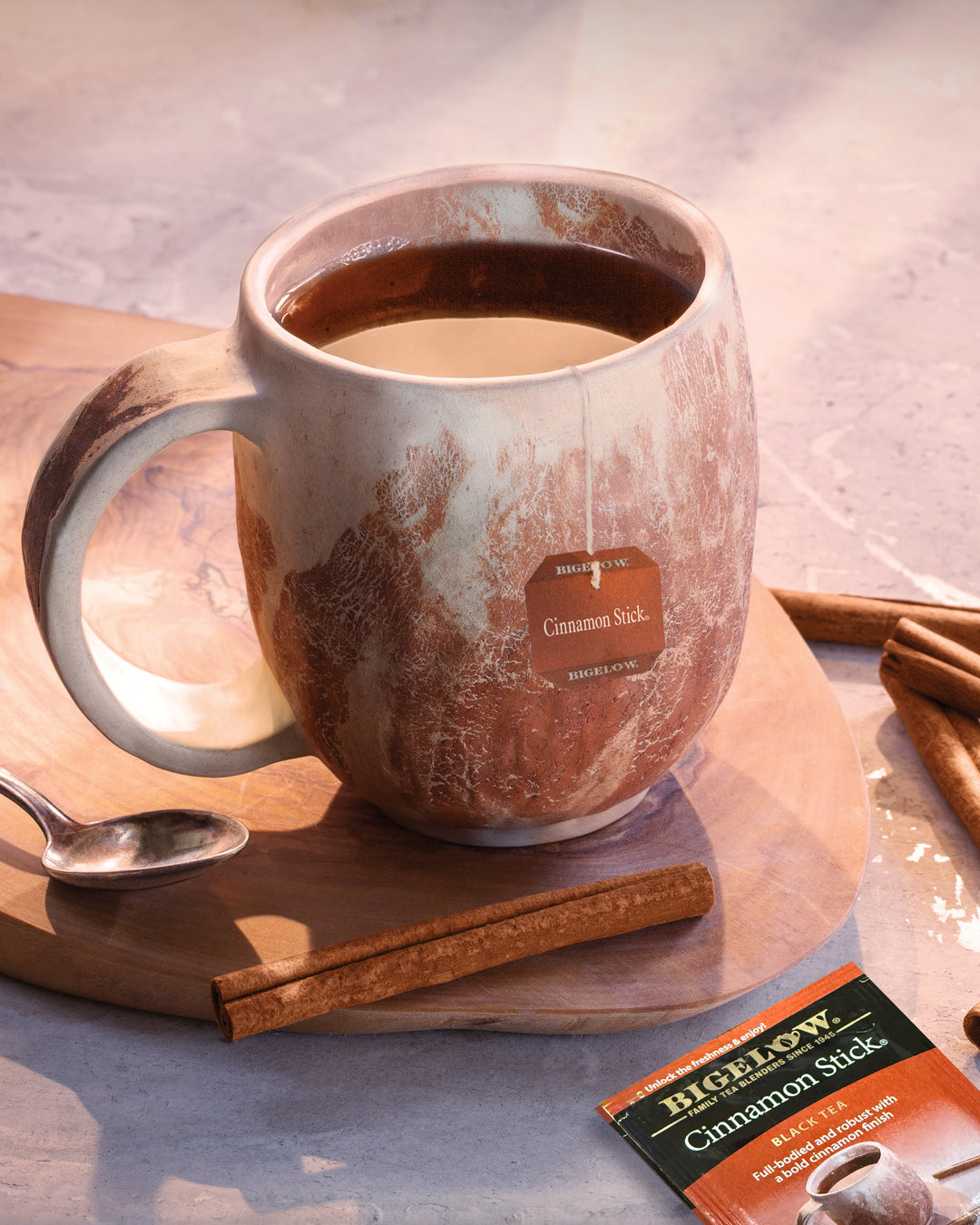 Mug of hot tea with a Bigelow Cinnamon Stick tea bag on a wooden board.