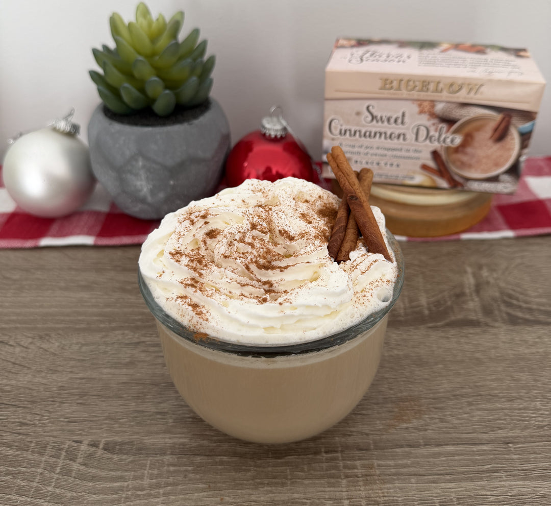 glass cup with latte and whipped cream with cinnamon sprinkling with box of Sweet Cinnamon Dolce Tea box in holiday setting