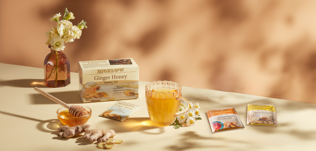 Bigelow honey teas with tea box and foils on table with honey in cup and on honey drizzler tool