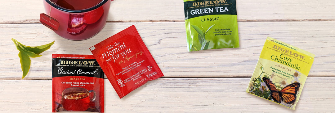 4 Bigelow Tea foil packets with red mug on white tabletop