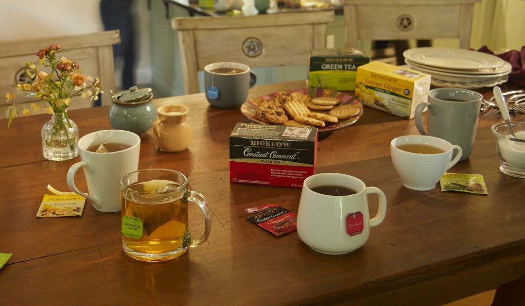 wooden table with cups of Bigelow Tea with cookies, flowers and boxes of Bigelow Tea
