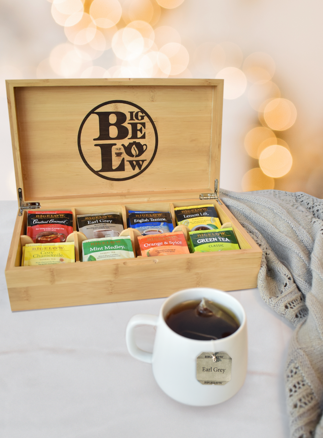 Bigelow Logo Wooden Tea Chest with 8 different teas in holiday lights background with cup of tea