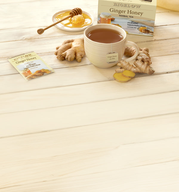 Ginger Honey Zinc tea box, foil and cup on white wood with ginger and honey ingredients laid out