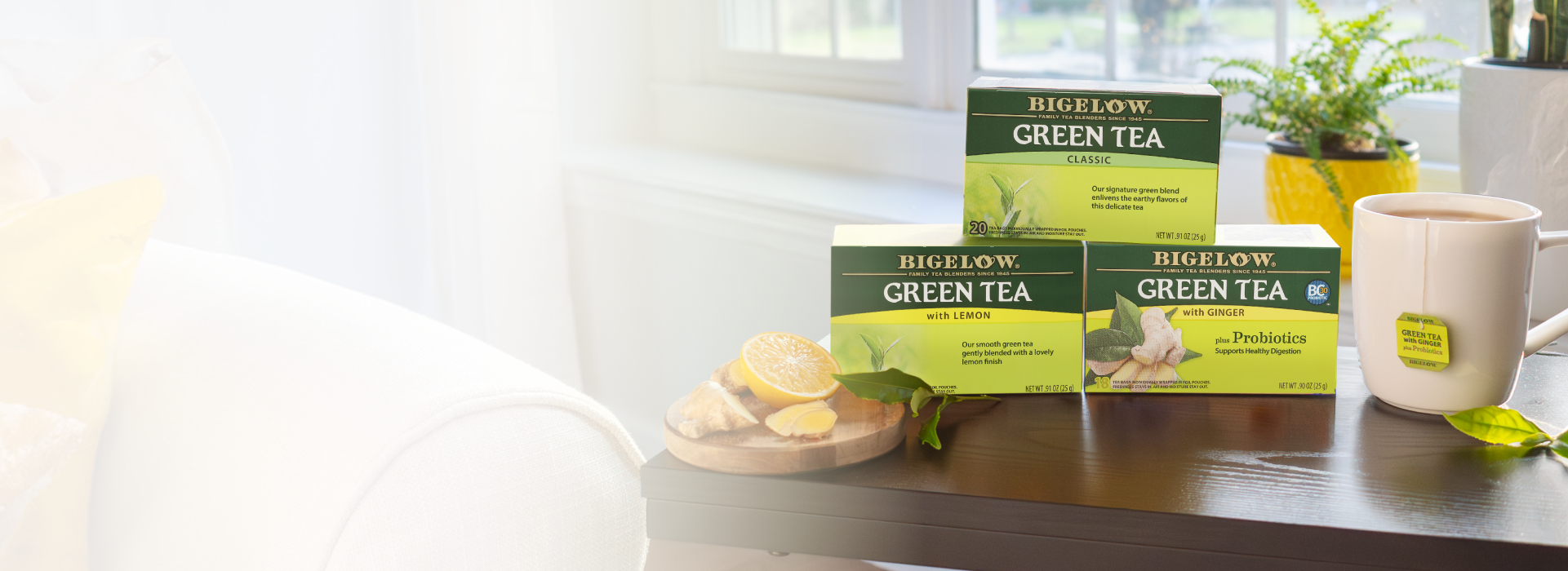 Bigelow Green Tea boxes on a table with a cup and lemon slices in a bright room.