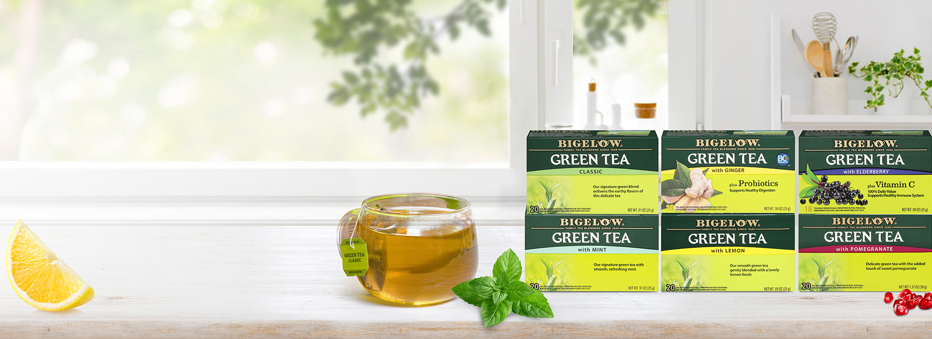 six boxes of green tea on whit e cabinet with drawers with glass cup of tea in front of window