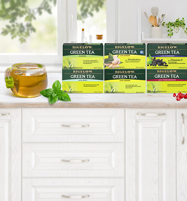 six boxes of green tea on whit e cabinet with drawers with glass cup of tea