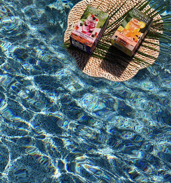 Two boxes of Bigelow Botanical Cold Water Infusions boxes Son a woven mat over clear blue water.