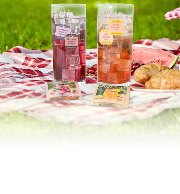 Two bottles of pink iced tea with a picnic setup on a blanket outdoors.