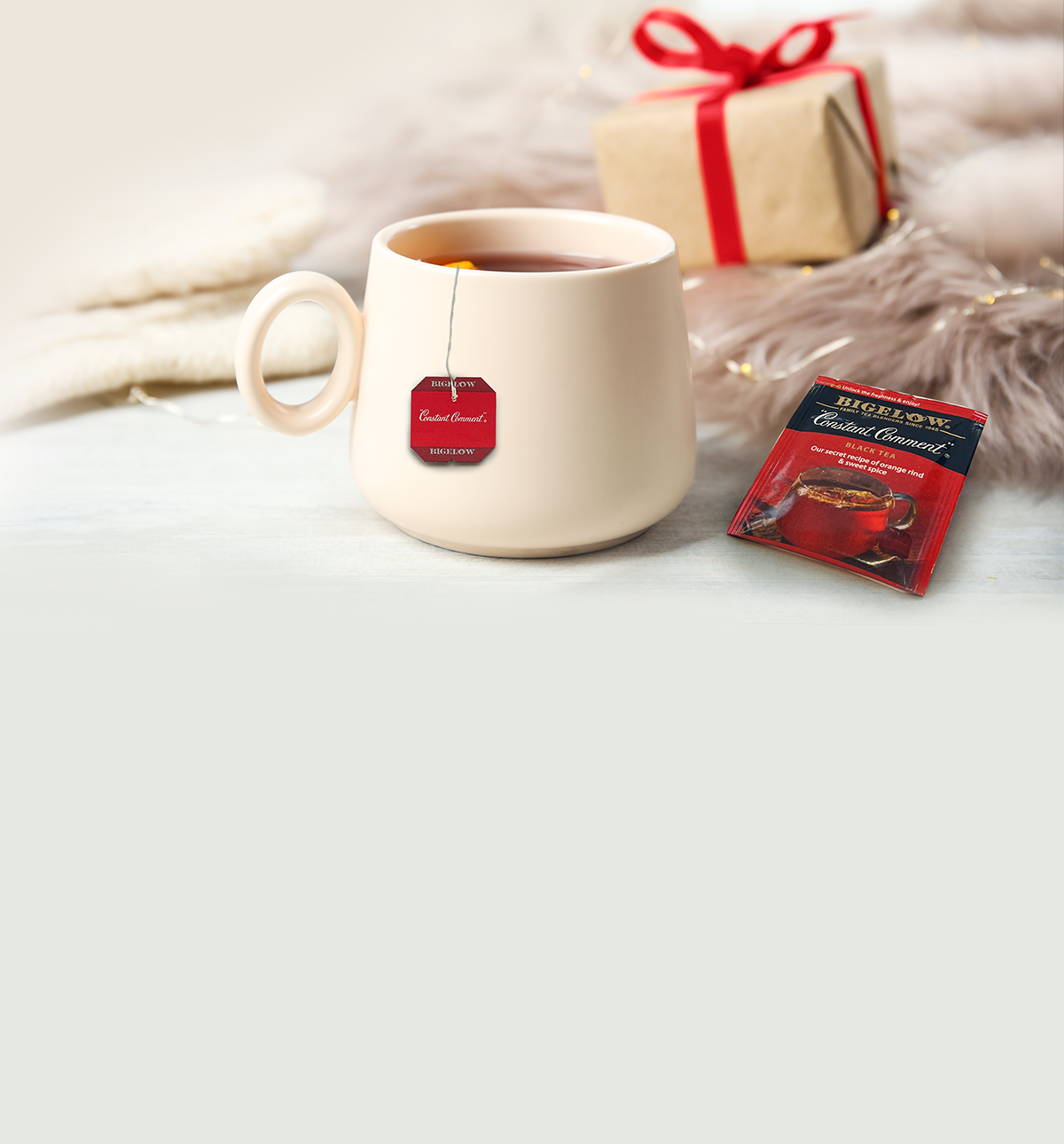 White mug with a tea bag label, Bigelow tea package, and gift box on a light surface.