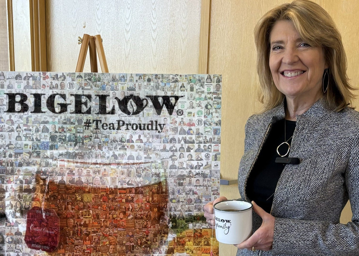 Woman holding a Bigelow tea cup in front of a Bigelow tea display.