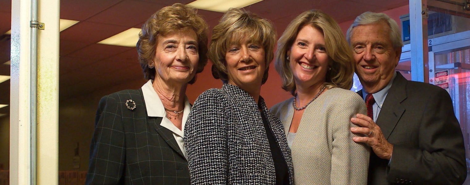 Four people posing together indoors. Two women and two men are standing side by side, smiling, with a warm-toned interior background featuring red and blue lighting.