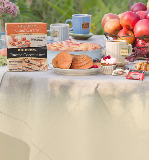 Table setting in a green field with2 boxes of Bigelow Dessert Teas with desserts, fruits and cups of tea