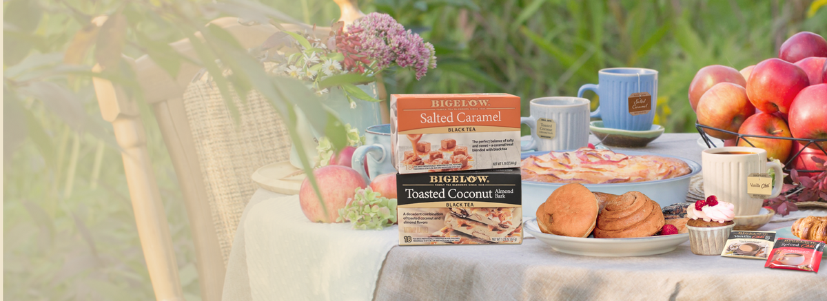 Table setting in a green field with2 boxes of Bigelow Dessert Teas with desserts, fruits and cups of tea