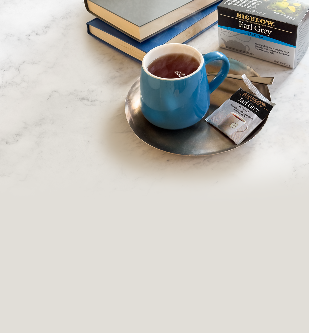 Blue mug with tea on a marble surface, surrounded by Bigelow Earl Grey tea packages.