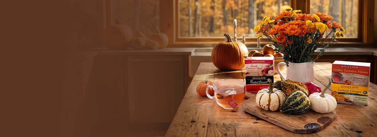 Wooden countertop with pumpkins and flowers and 4 boxes of Bigelow Tea with a glass cp of tea
