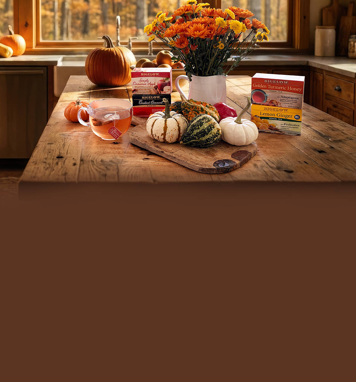 Wooden countertop with pumpkins and flowers and 4 boxes of Bigelow Tea with a glass cp of tea
