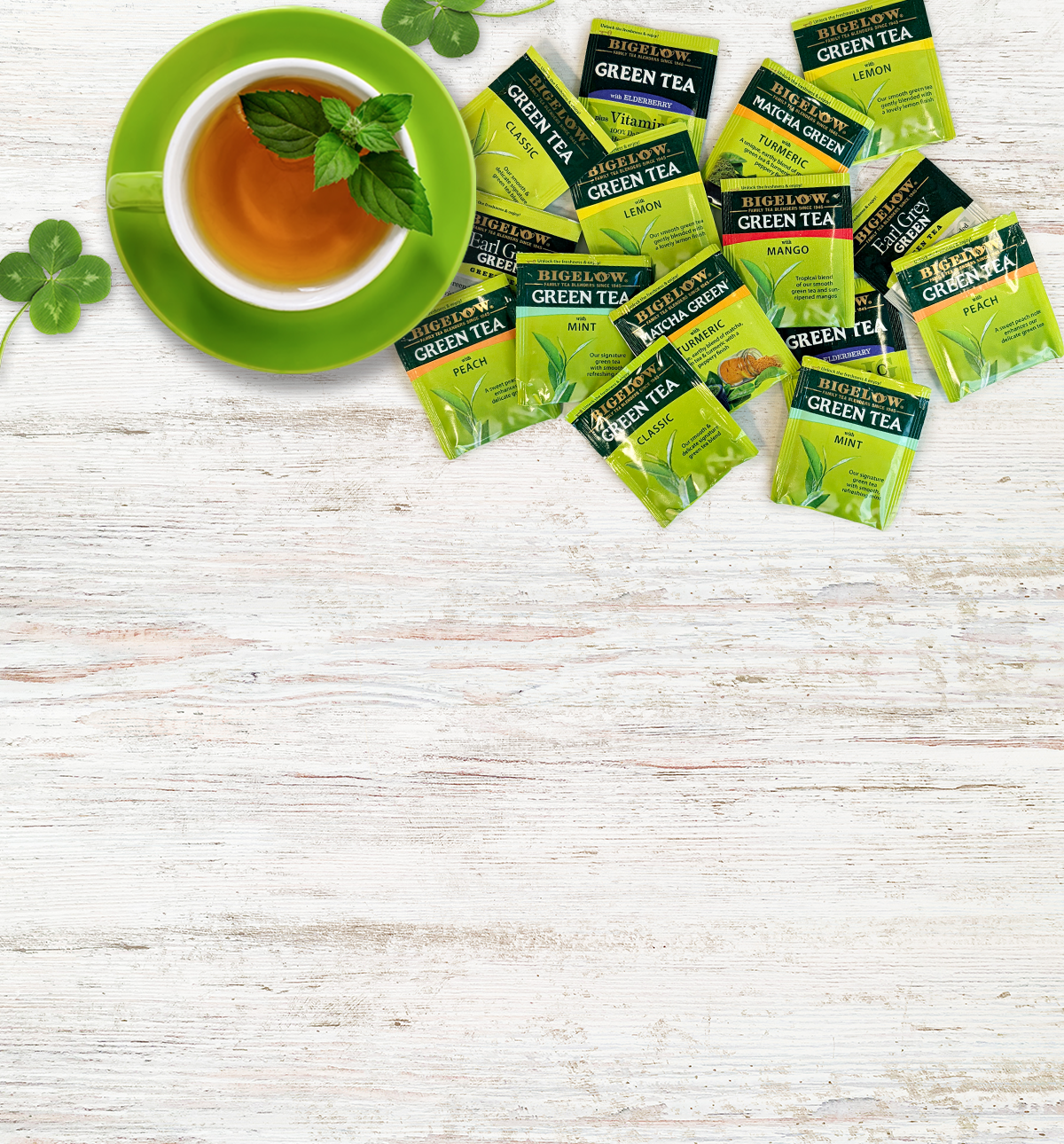Green tea packets and a cup of tea on a white wooden surface