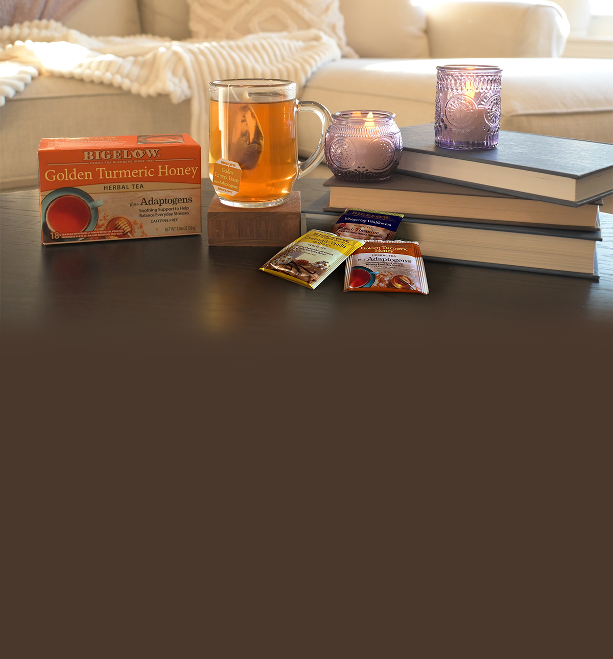 Bigelow Golden Turmeric Tea box and glass mug of tea on table with candles and books in a living room setting