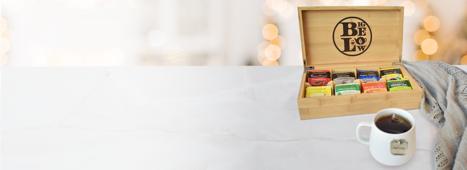 Tea box with assorted tea bags and a cup of coffee on a white surface with a blurred background.