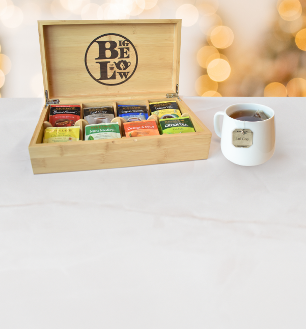 Tea box with assorted tea bags and a cup of tea on a white surface.