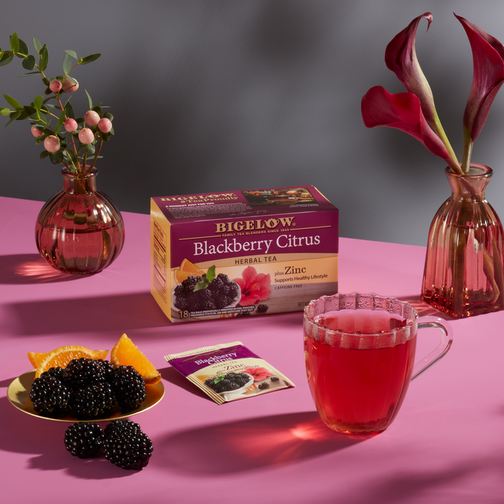 Glass mug of Blackberry Citrus Herbal Tea with box, with ingredients on grey cloth