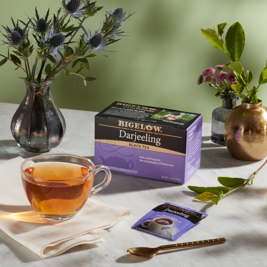 Cup of Darjeeling Tea with box and foil packet on white table with 2 floral vases
