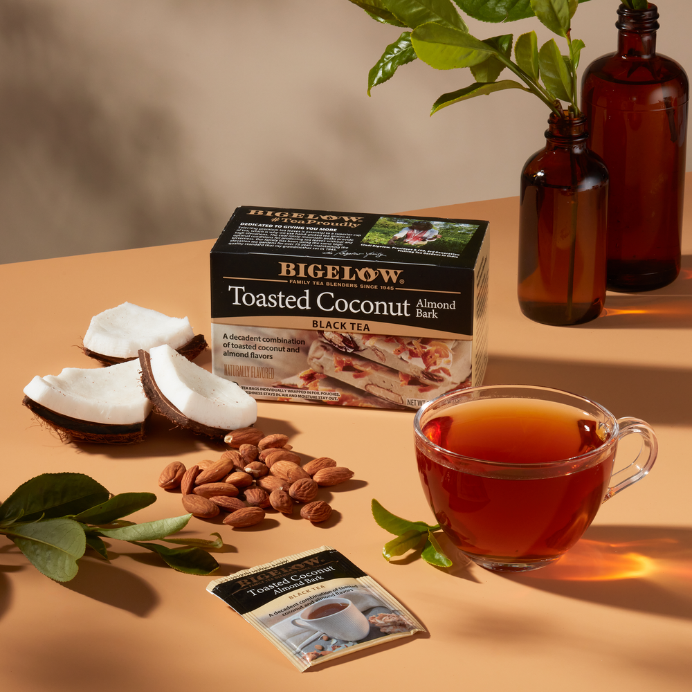 Glass cup of Toasted Coconut Almond Bark Tea on table with box and foil packet along with coconut pieces and almonds