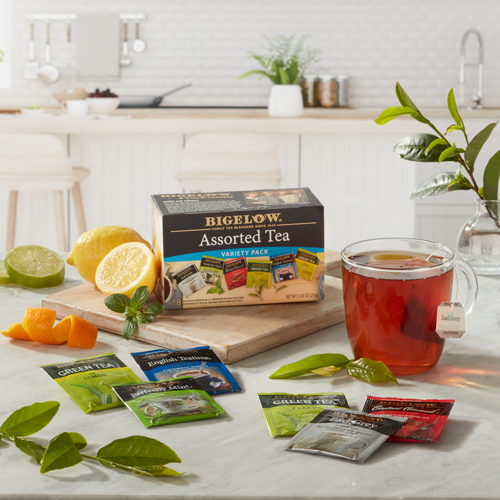 Box of Bigelow Assorted Tea Variety with glass mug and foil packets in kitchen setting