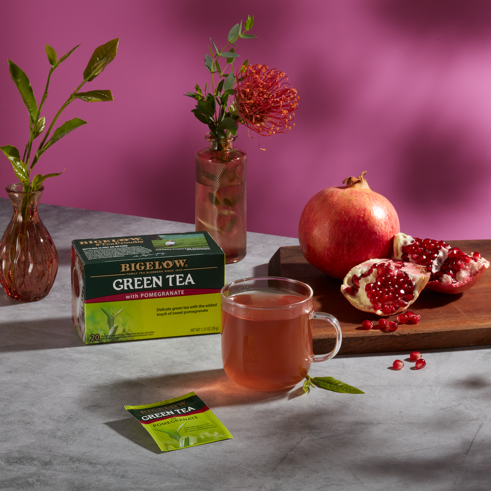 Glass mug of Green Tea with Pomegranate with box, with ingredients on grey cloth