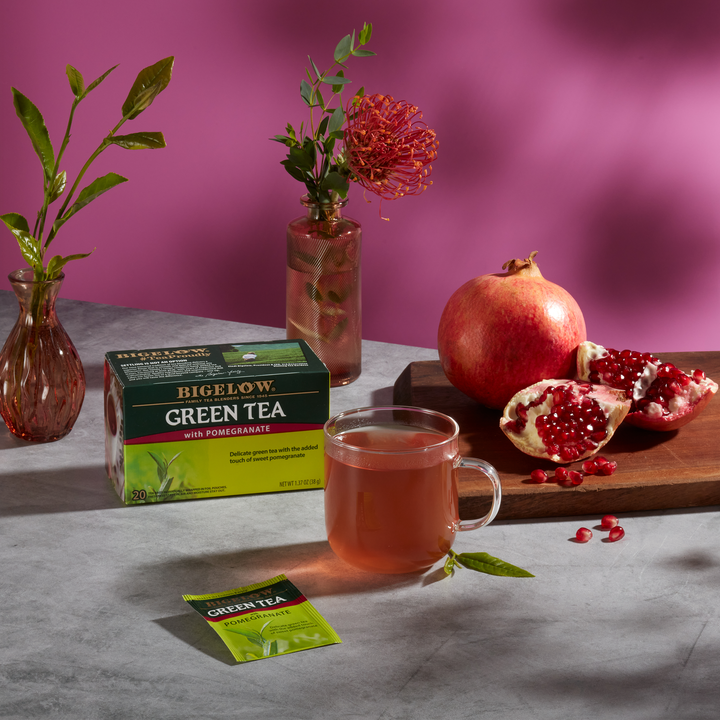 Glass mug of Green Tea with Pomegranate with box, with ingredients on grey cloth