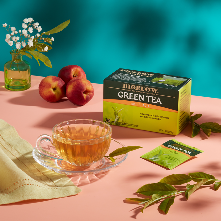 Glass cup of Green Tea with Peach with foil packet on pink cloth with teal blue background