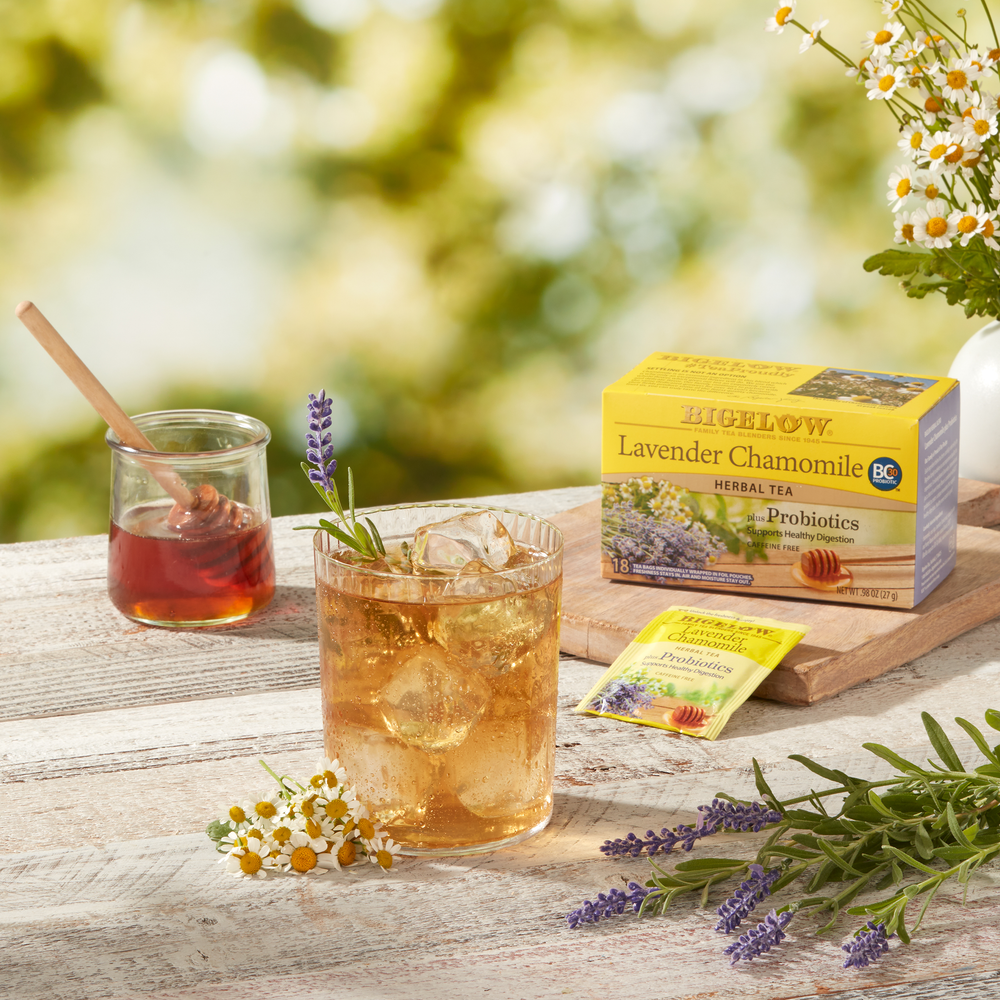 Glass of Lavender Chamomile Plus Probiotics Herbal Tea over ice with a jar of honey and flowers on a wood board