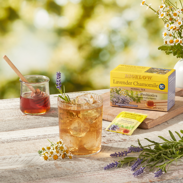 Glass of Lavender Chamomile Plus Probiotics Herbal Tea over ice with a jar of honey and flowers on a wood board