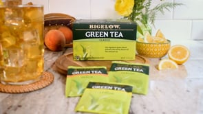 Glass filled with iced and iced green Bigelow tea with tea boxes and lemons