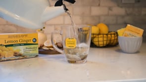 pouring water from white kettle into glass cup with box of Bigelow Lemon Ginger Tea