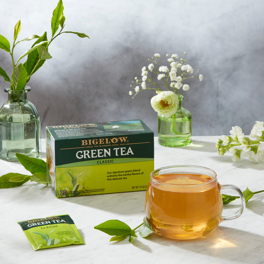 Glass mug of Green Tea Classic with box, with ingredients on light grey cloth