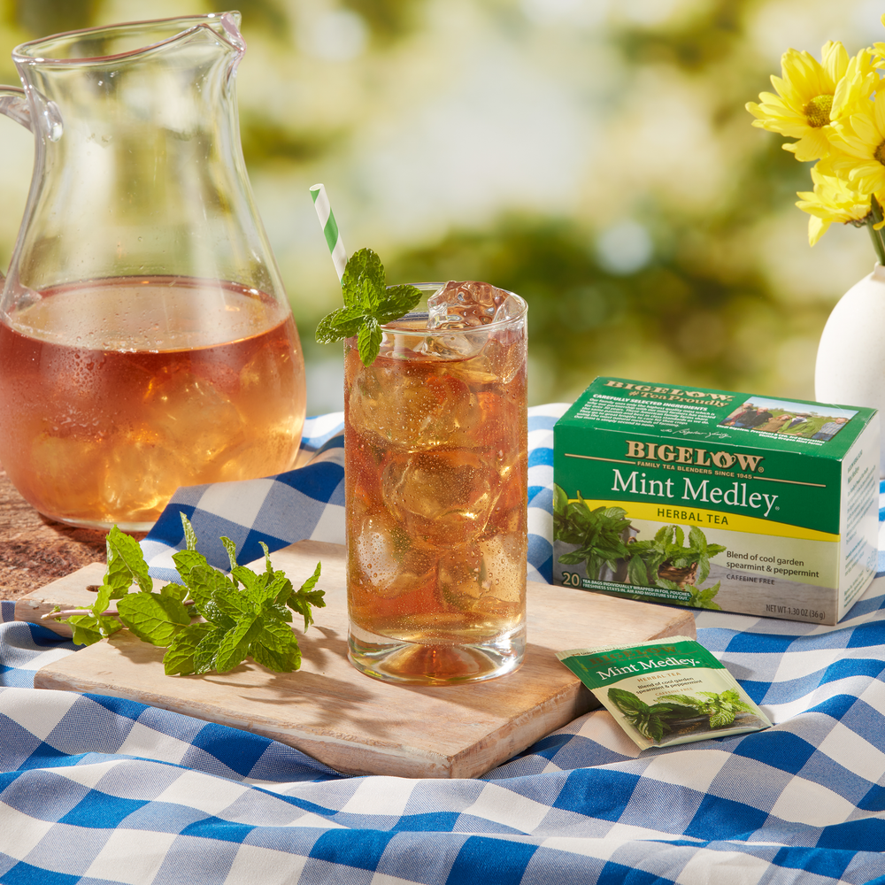 Glass pitcher and cup of Mint Medley Herbal Iced Tea on blue checkered table cloth