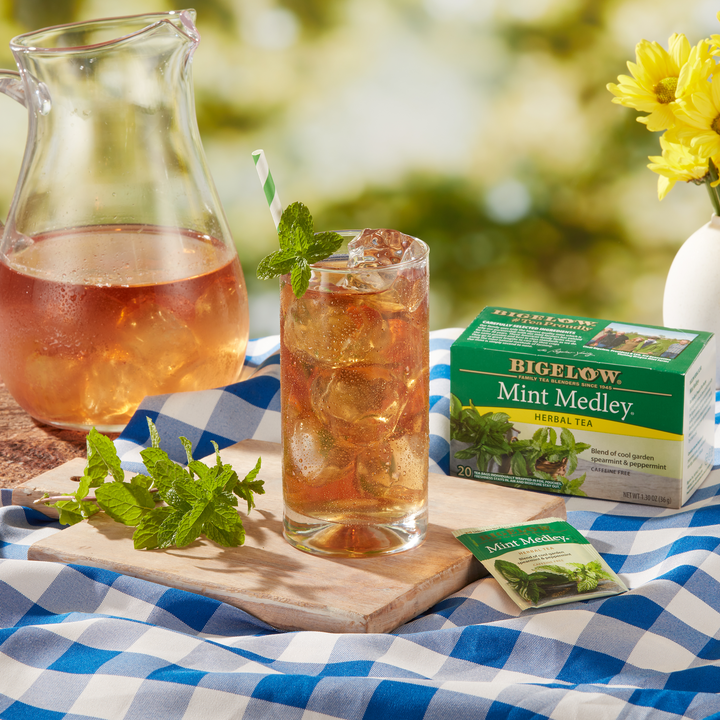 Glass pitcher and cup of Mint Medley Herbal Iced Tea on blue checkered table cloth