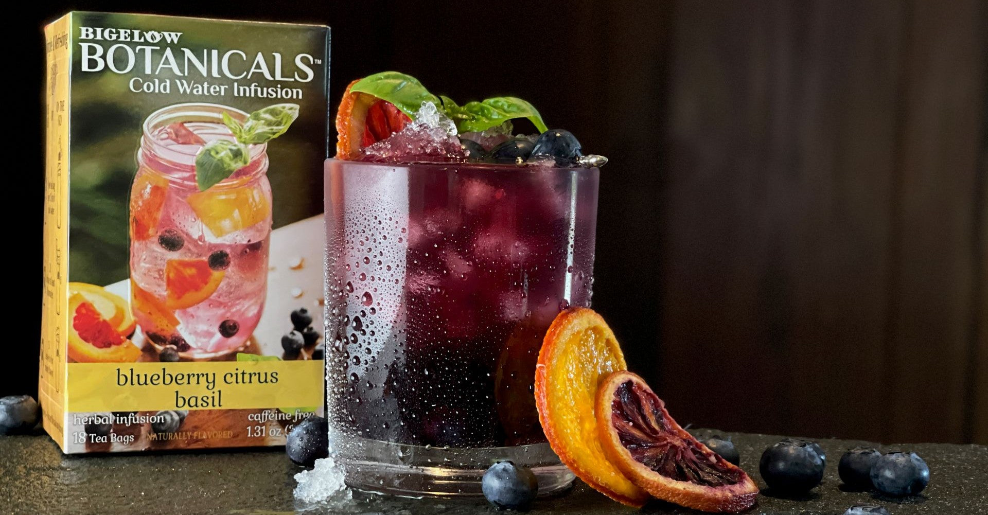 Cold water infusion with botanicals packaging and garnished drink on a dark surface