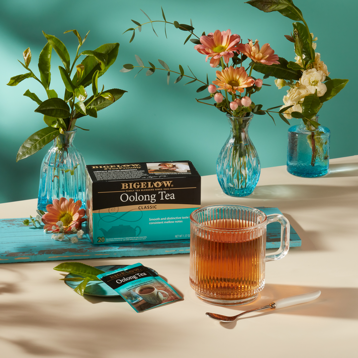 Glass Cup of Oolong Tea with box and foil and three vases of flowers on table