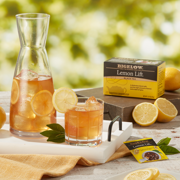 Carafe and glass of Iced  Lemon Lift Tea with box and foil packet in a garden setting