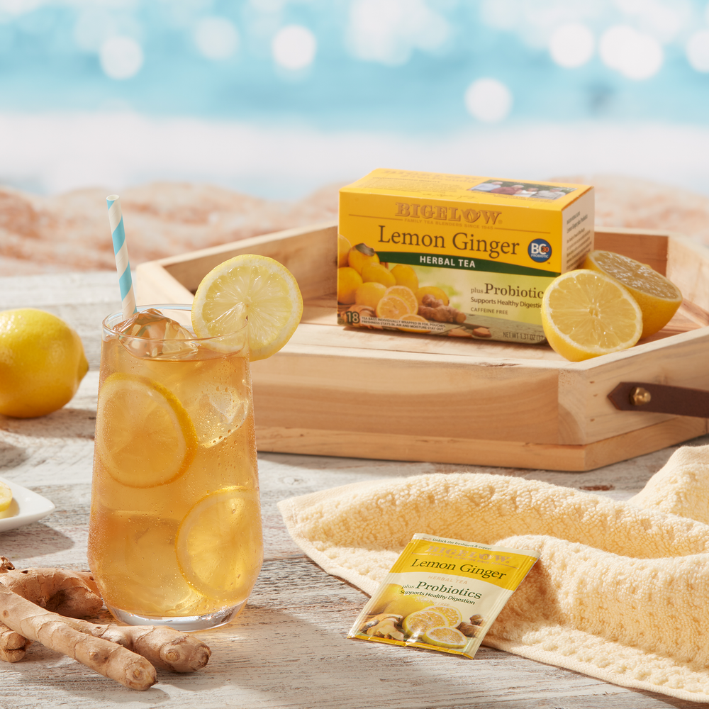 Beach scene with a box of Bigelow Lemon Ginger Plus Probiotics tea with lemons and a glass of Lemon Ginger Iced tea