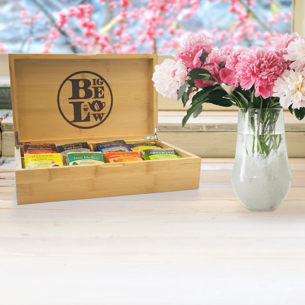 Tea chest with 'BIGELOW' branding on a table with flowers in the background