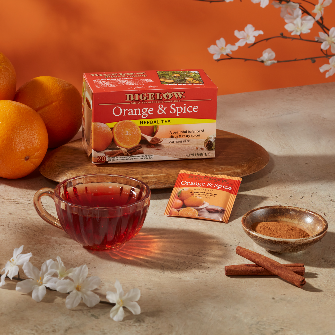 Glass cup of Orange and Spice Herbal Tea with box and foil on creme countertop with oranges and cinnamon sticks