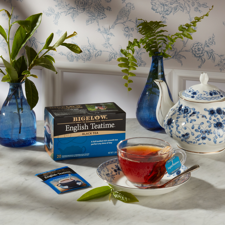 Glass cup  of English Teatime with box, with ingredients and blue and white teapot on white cloth with printed background