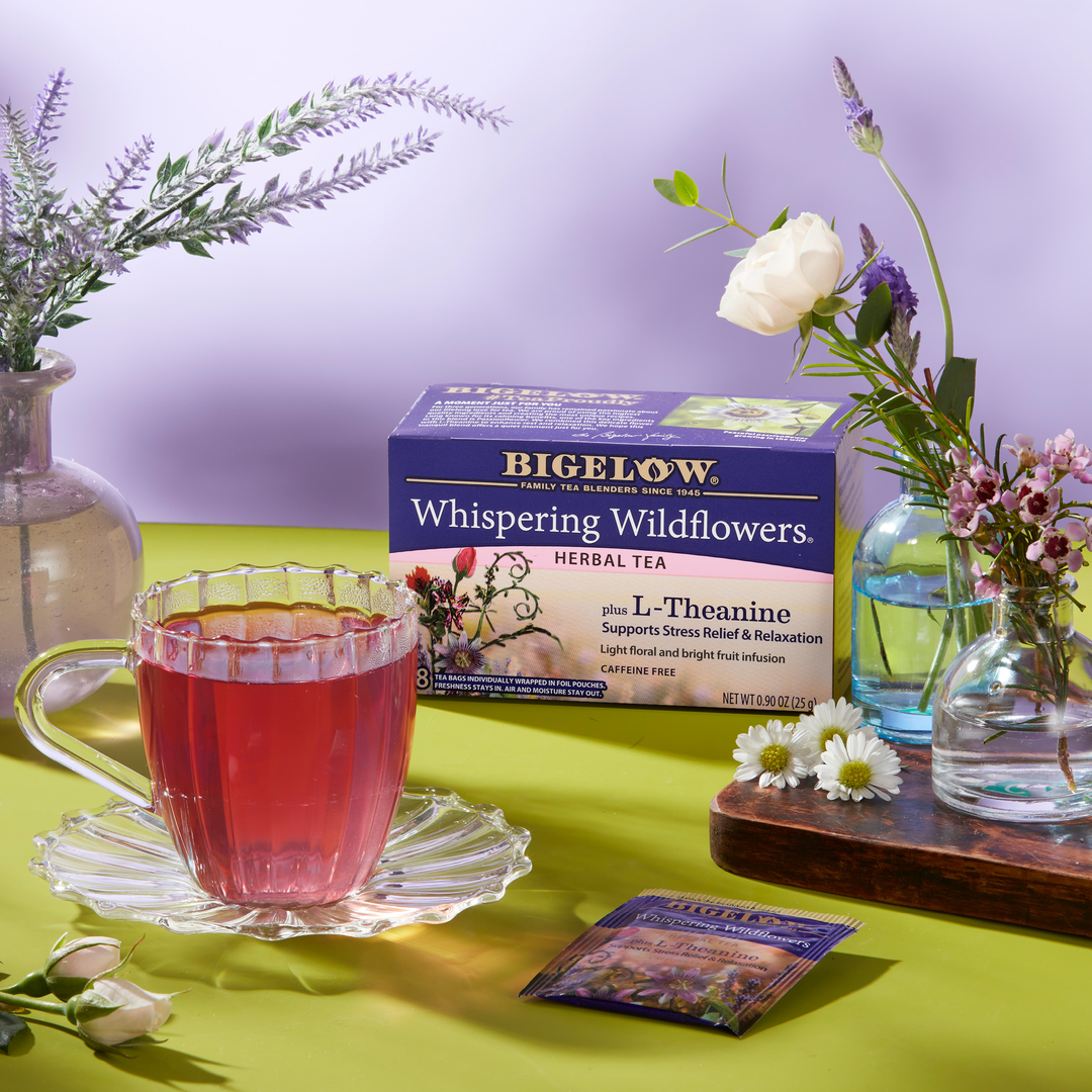 Bigelow Whispering Wildflowers herbal tea with a cup of tea on a green surface with flowers.