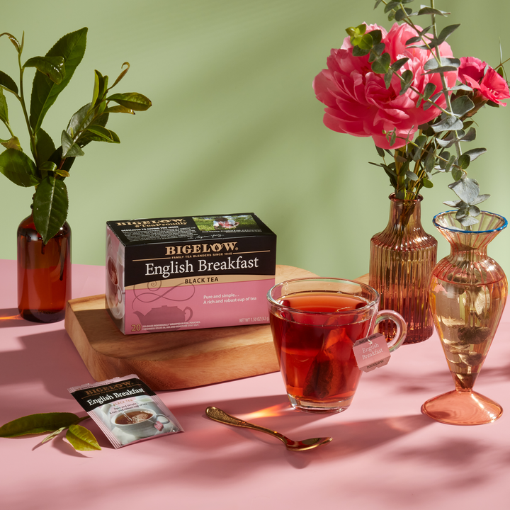 Glass mug of English Breakfast Tea with box and foil packet on pink cloth with green background