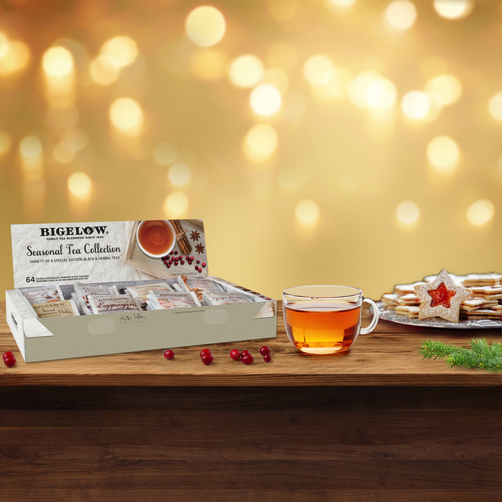 Bigelow tea collection with a cup of tea and cookies on a wooden surface with a warm, blurred background.
