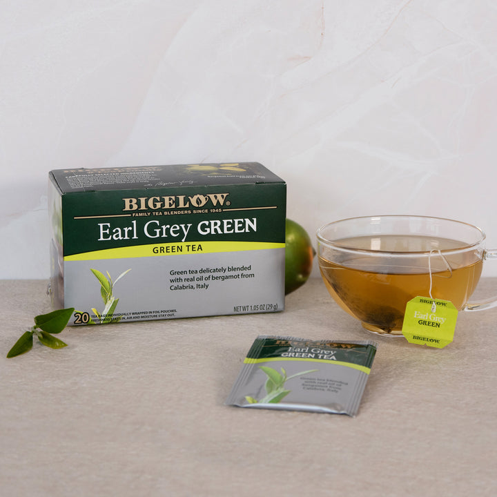 Bigelow Earl Grey Green tea box with a cup of tea and a tea bag on a light surface.